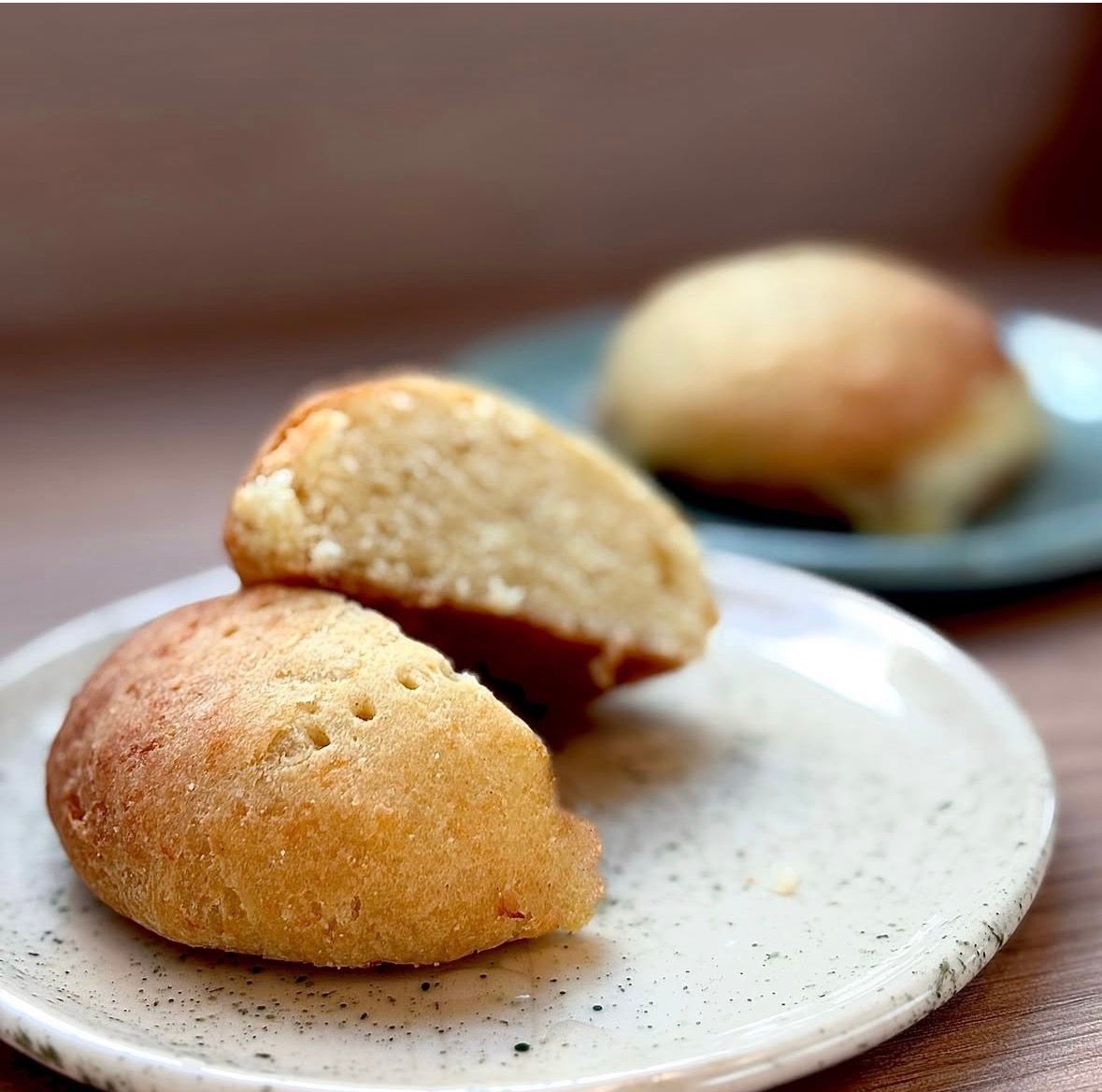 Dos panecillos horneados de color dorado, uno de ellos cortado para revelar un interior suave, se encuentran sobre un plato blanco.