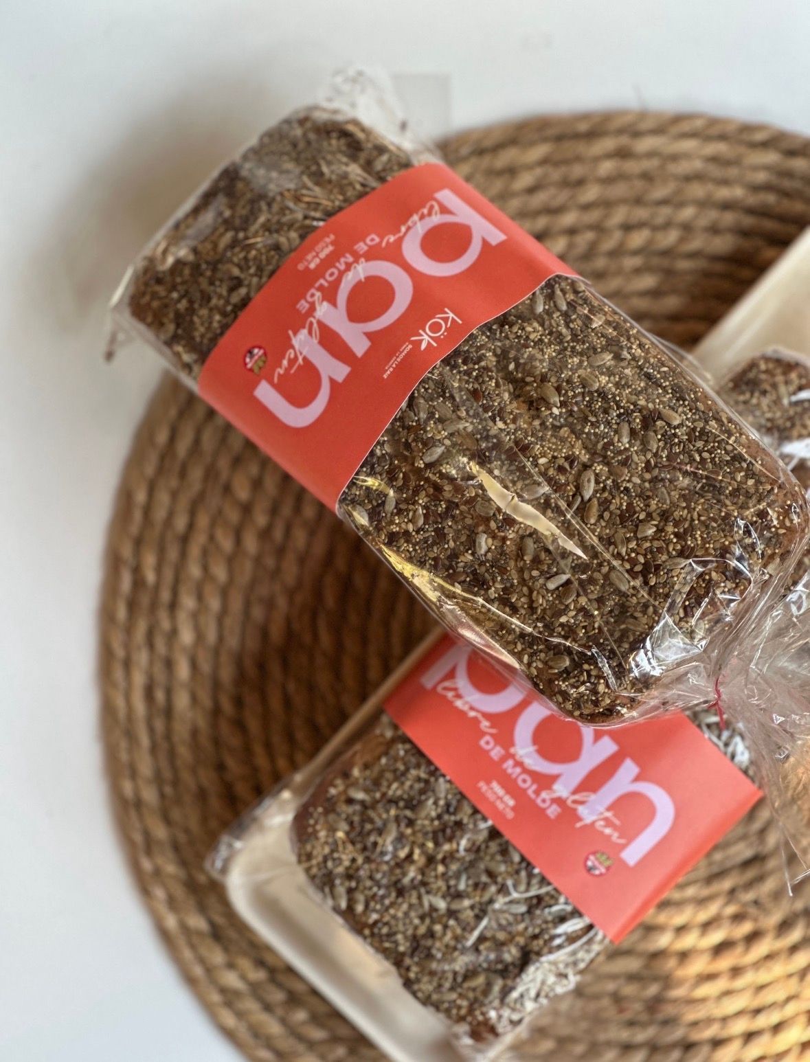 Dos hogazas de pan envasado, con etiqueta naranja, sobre una estera tejida.