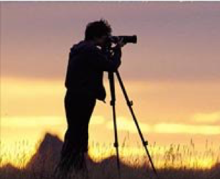 Silhouette of photographer with camera on tripod at sunset.