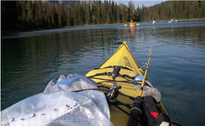 Yellow kayak on calm water, fishing rod, other kayaks and trees in the background.