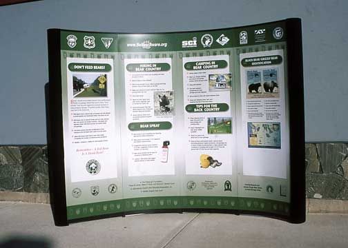 Curved green and black information board with text and graphics. Outdoor setting.