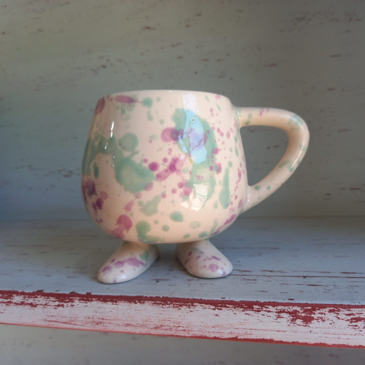 Una taza colorida con asa y patas se encuentra en un estante.