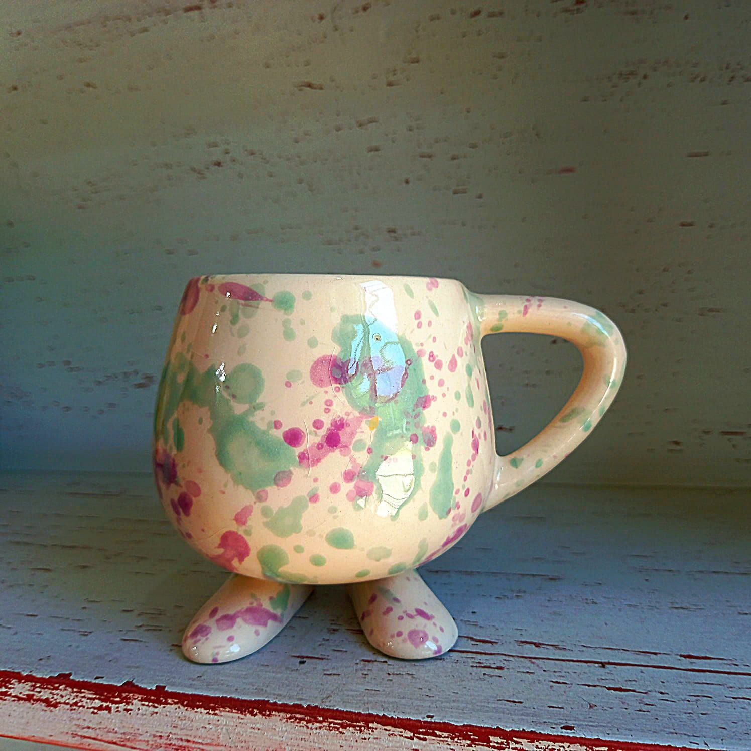 Una taza colorida con asa y patas se encuentra en un estante.