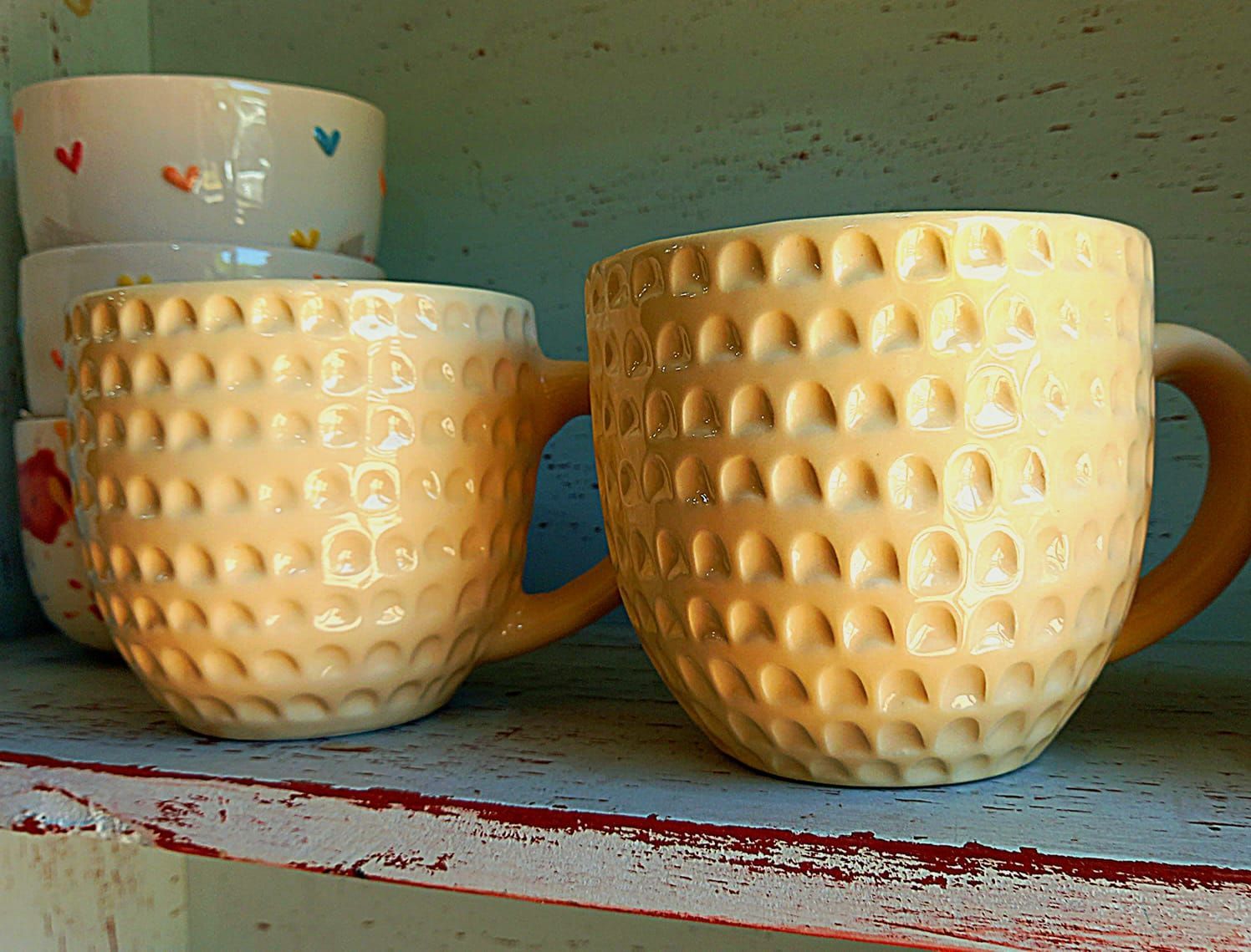 Un par de tazas colocadas en un estante junto a una pila de tazones.