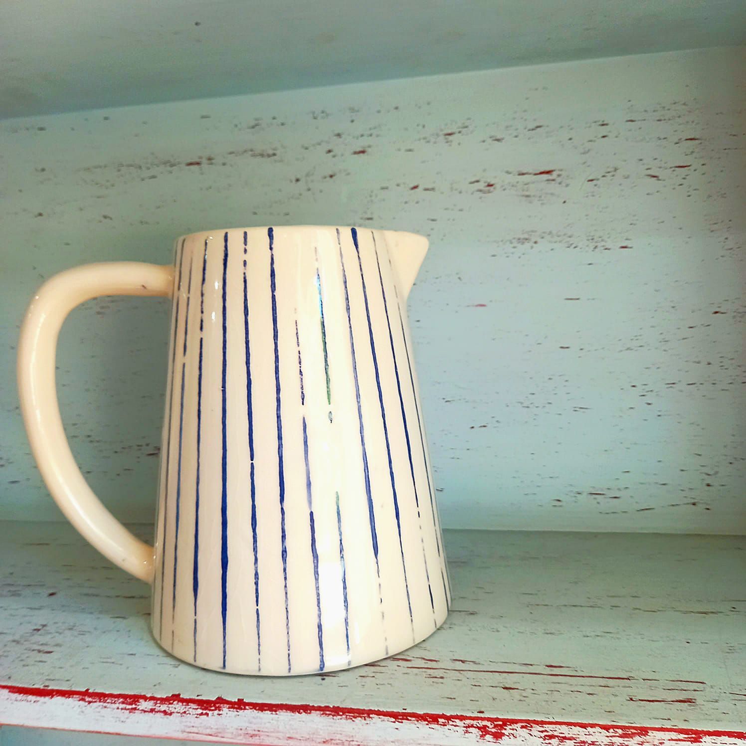 Una jarra y dos tazas están en un estante.