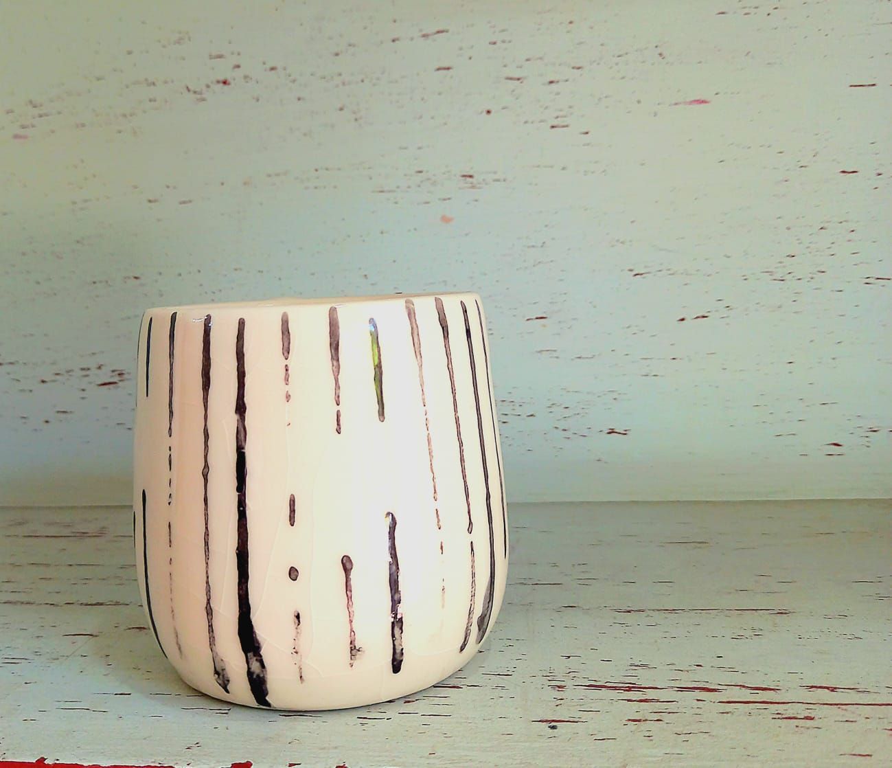 Un jarrón de rayas se encuentra sobre un estante de madera.