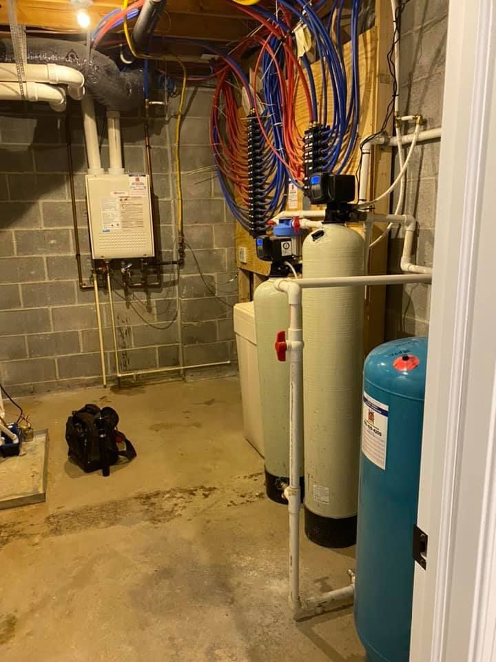 A stainless steel water heater is sitting in a basement next to a wall.