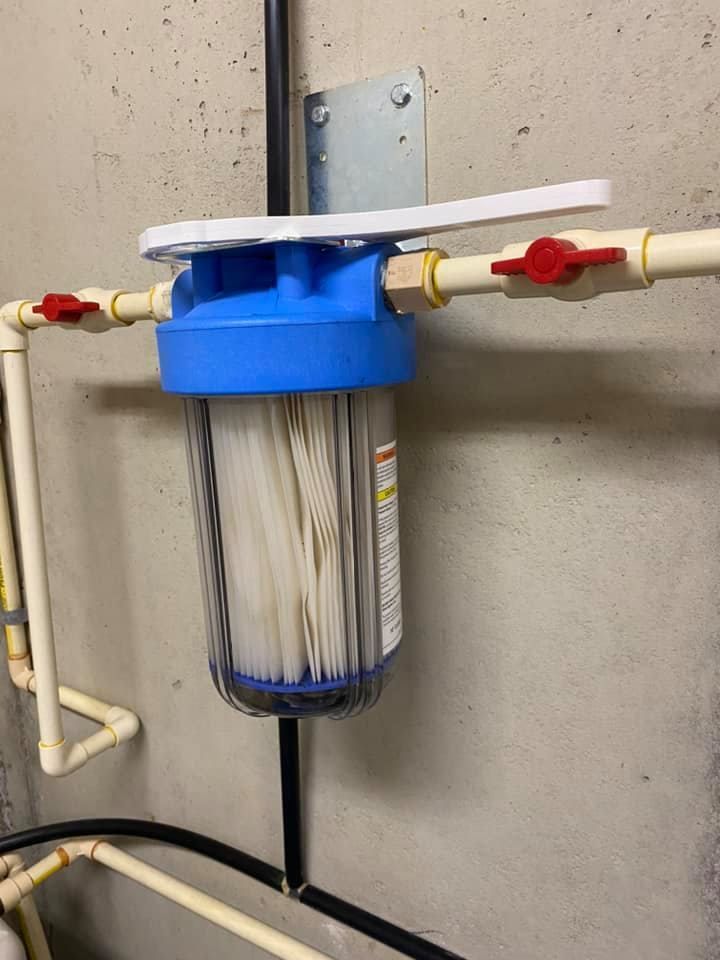 A water filter is hanging on a wall next to pipes.
