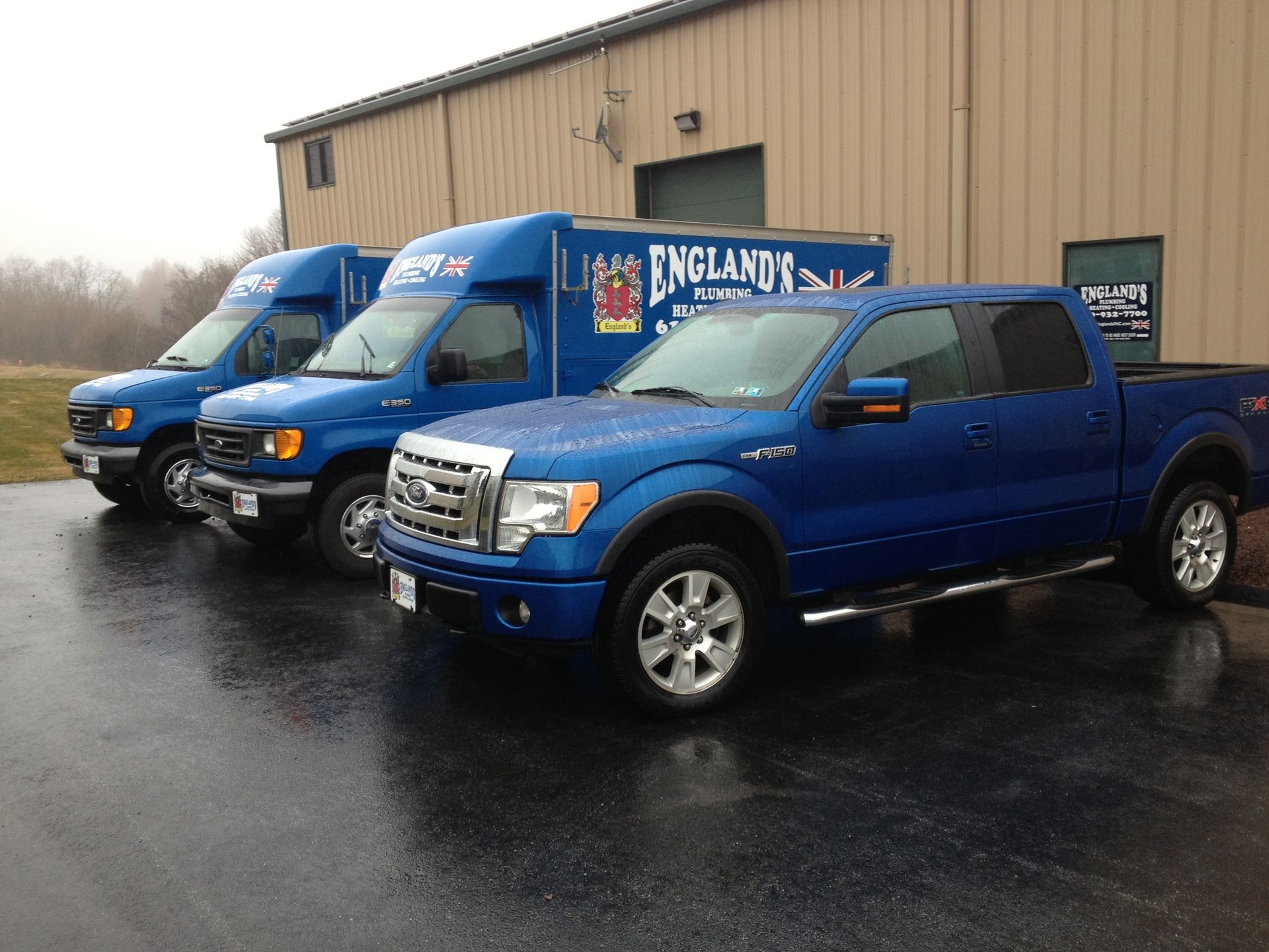 Three blue trucks are parked in front of a building that says england