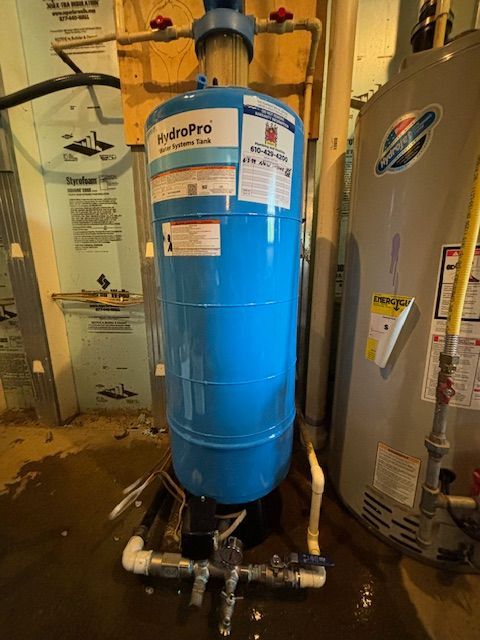 A blue water tank is sitting next to a water heater in a basement.