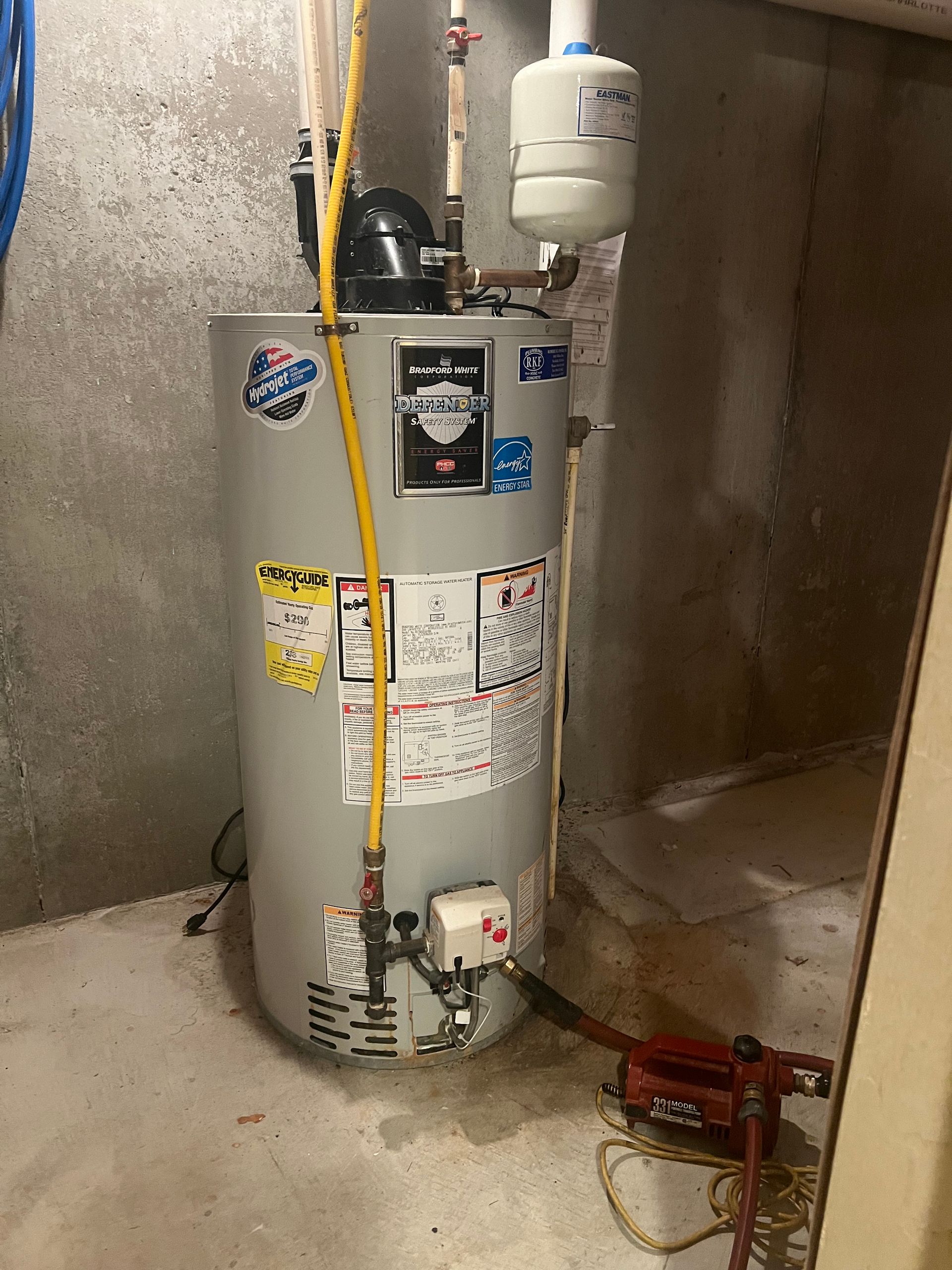 A water heater is sitting in a basement next to a wall.