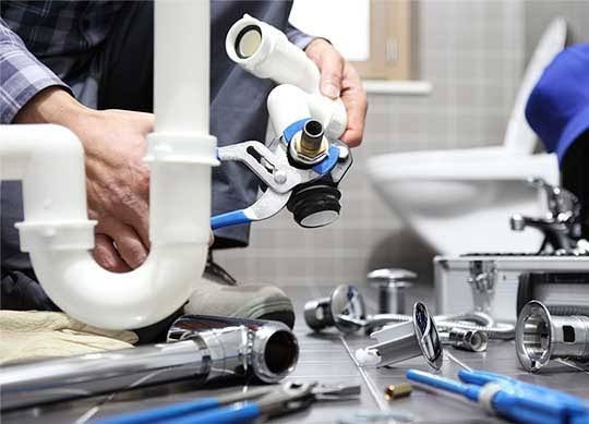 A plumber is working on a sink pipe in a bathroom.