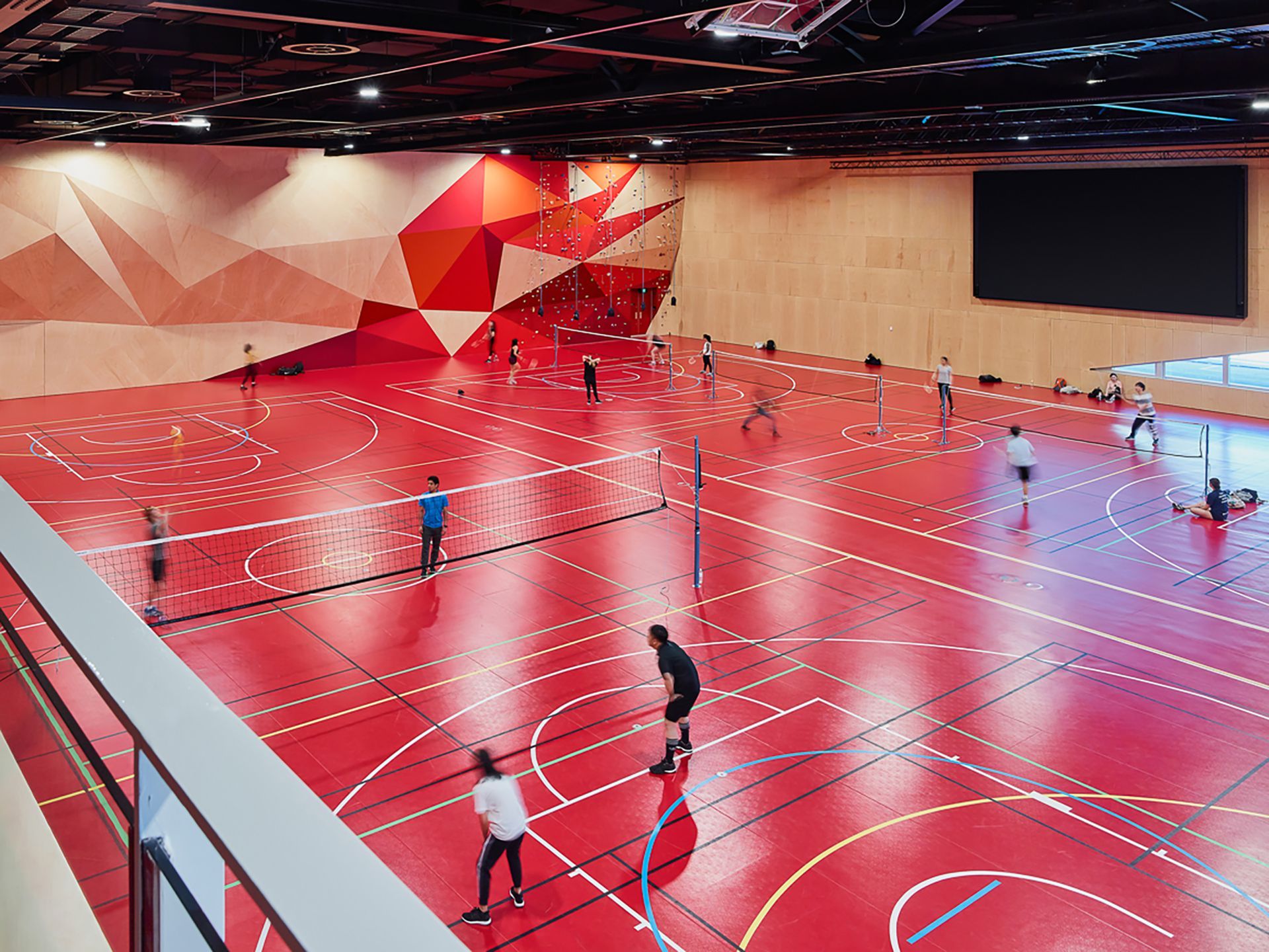 A group of people are playing volleyball on a red court.