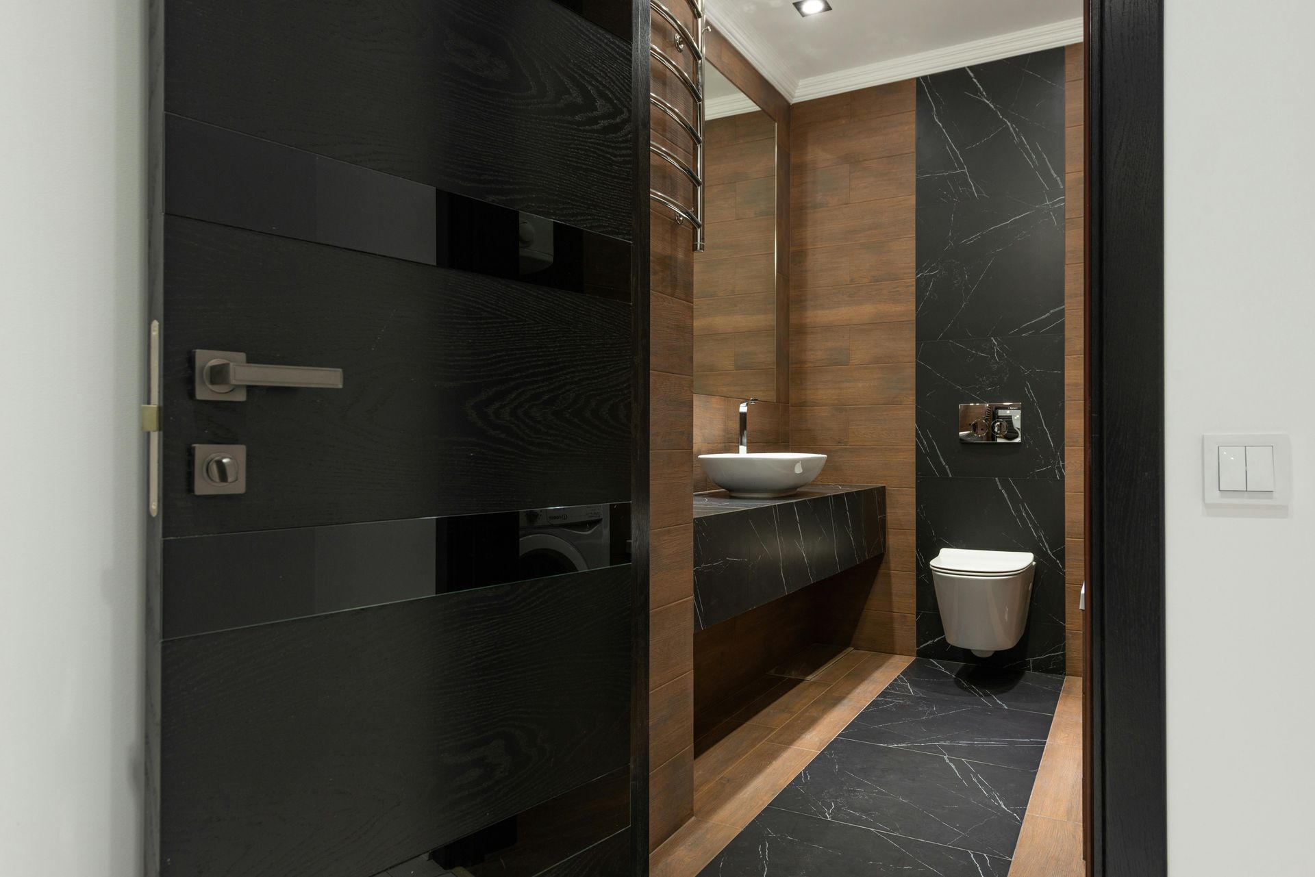 A bathroom with a black door , a sink , a toilet and a mirror.