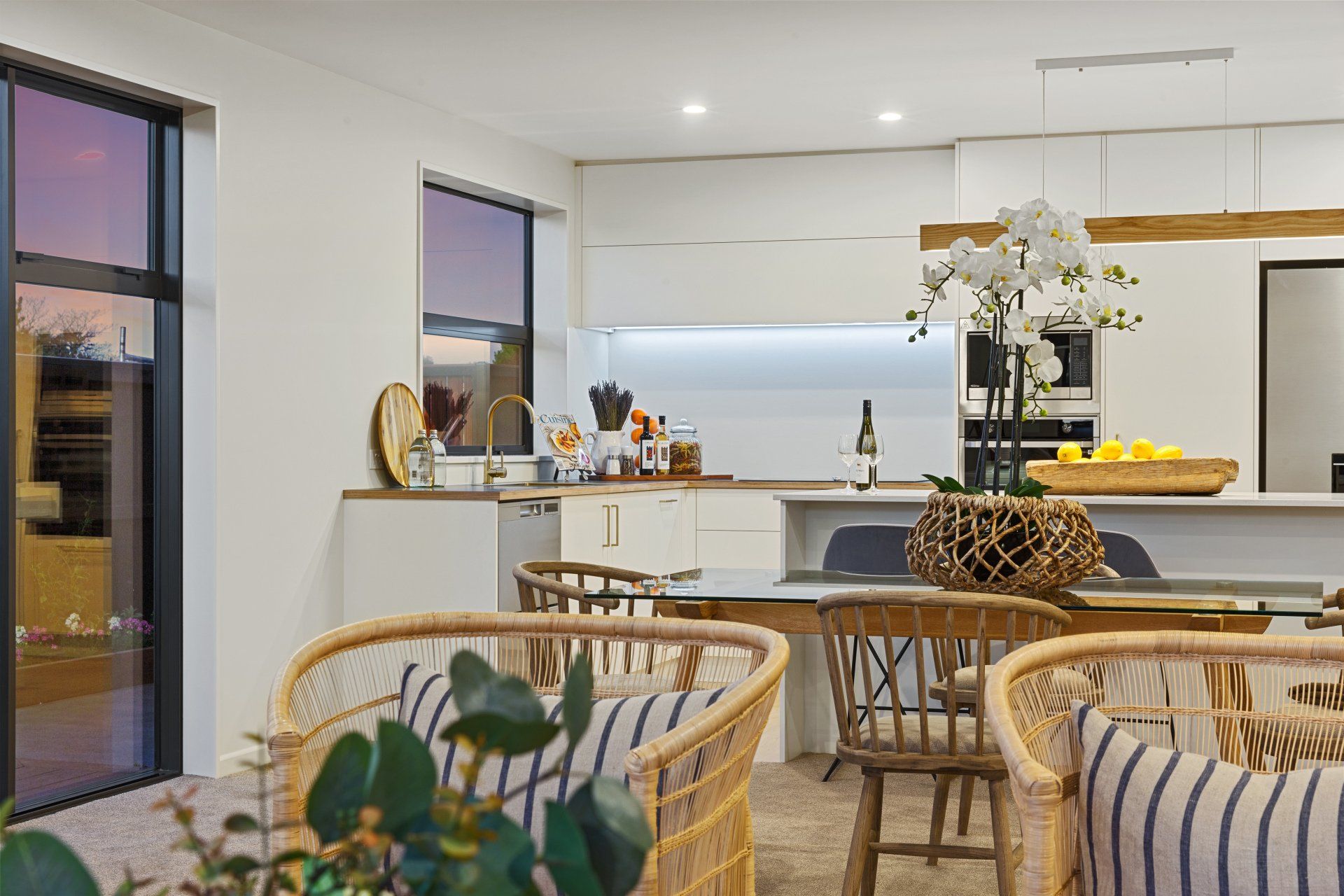 A living room with a table and chairs and a kitchen in the background.