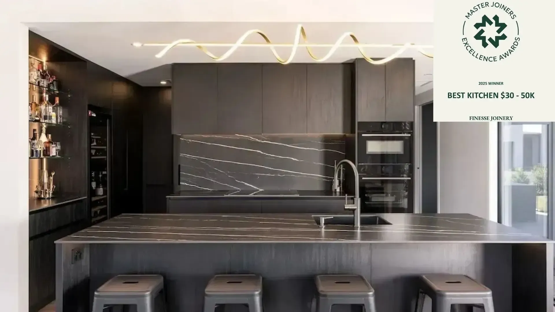 Dark modern kitchen with black cabinetry, island, stools, and light fixture.