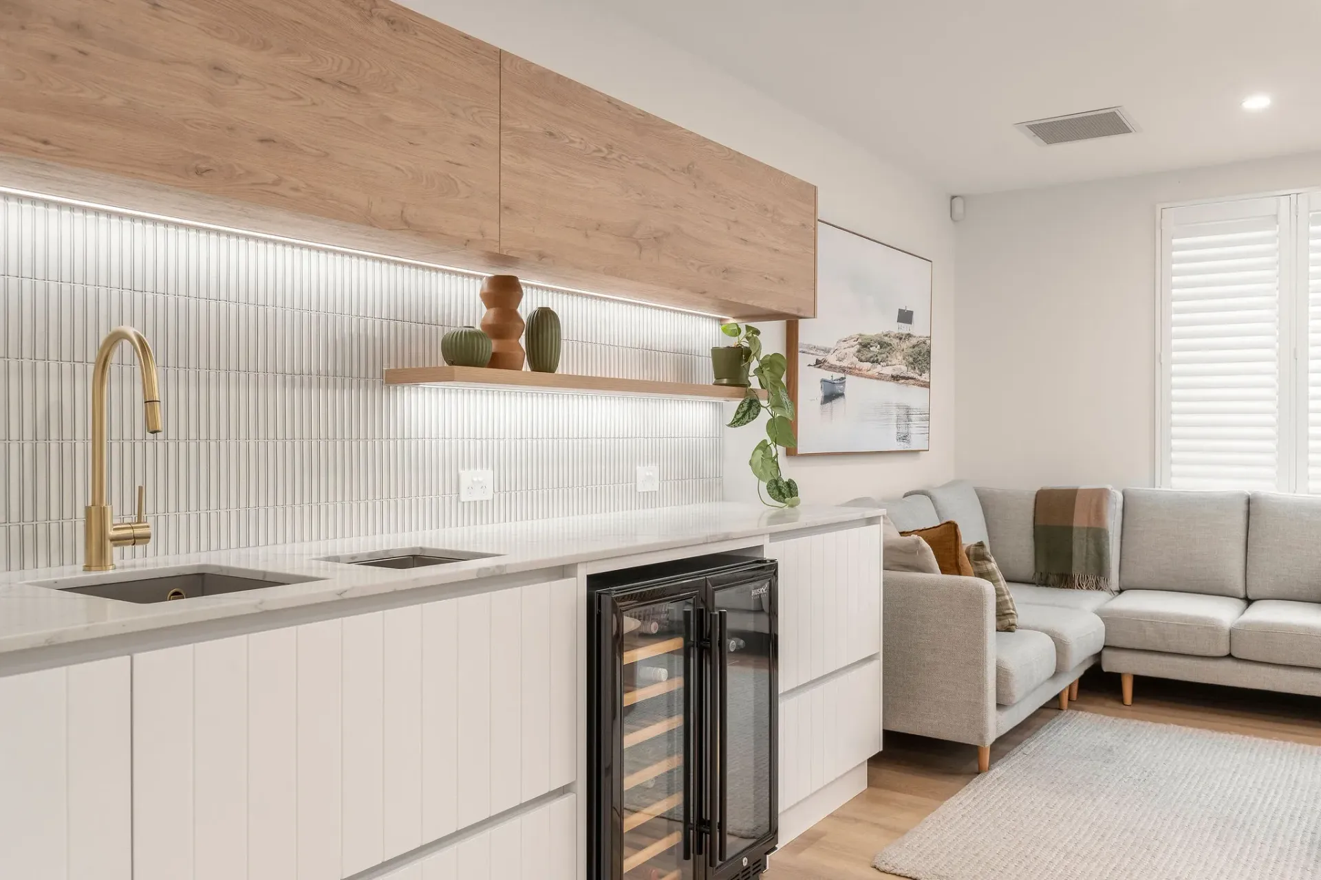 A living room with a couch and a kitchen with a wine cooler.