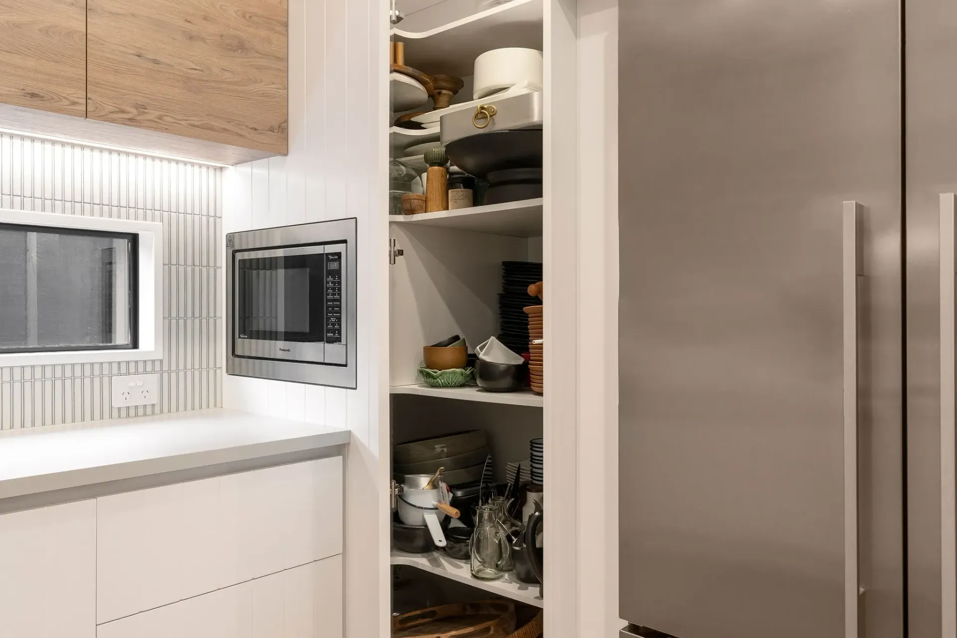 A kitchen with a refrigerator , microwave , and pantry.