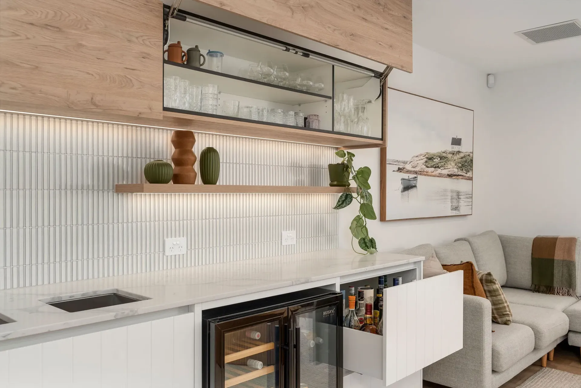 A kitchen with a wine cooler and a couch in the background.