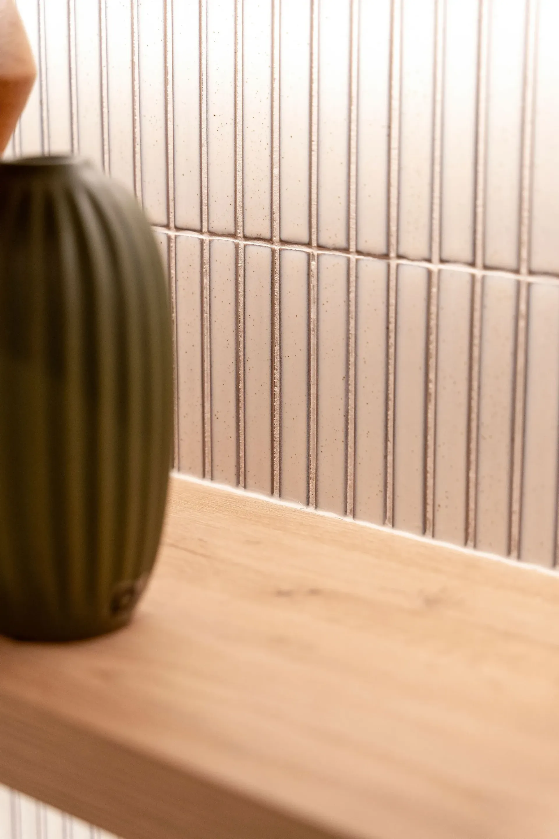 A green vase is sitting on a wooden shelf next to a lamp.