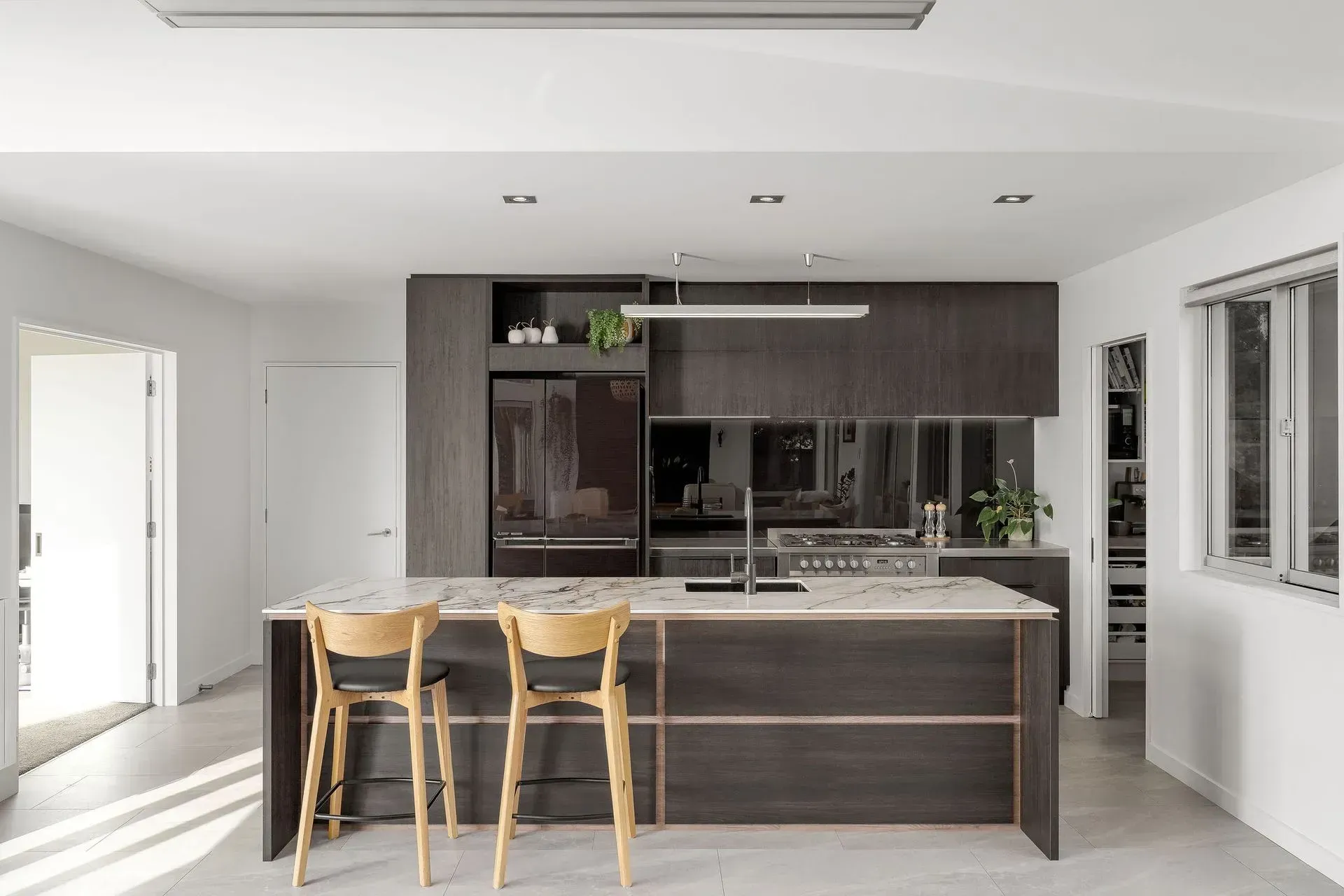 A kitchen with a refrigerator and a pantry with bottles and glasses on the shelves.