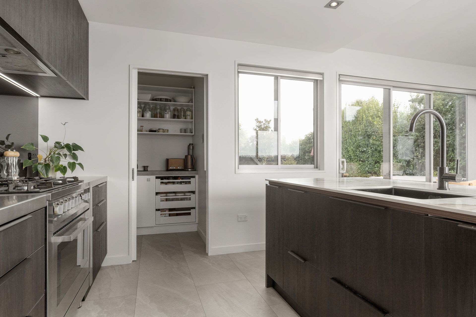 A kitchen with stainless steel appliances , wooden cabinets , a sink , and a pantry.