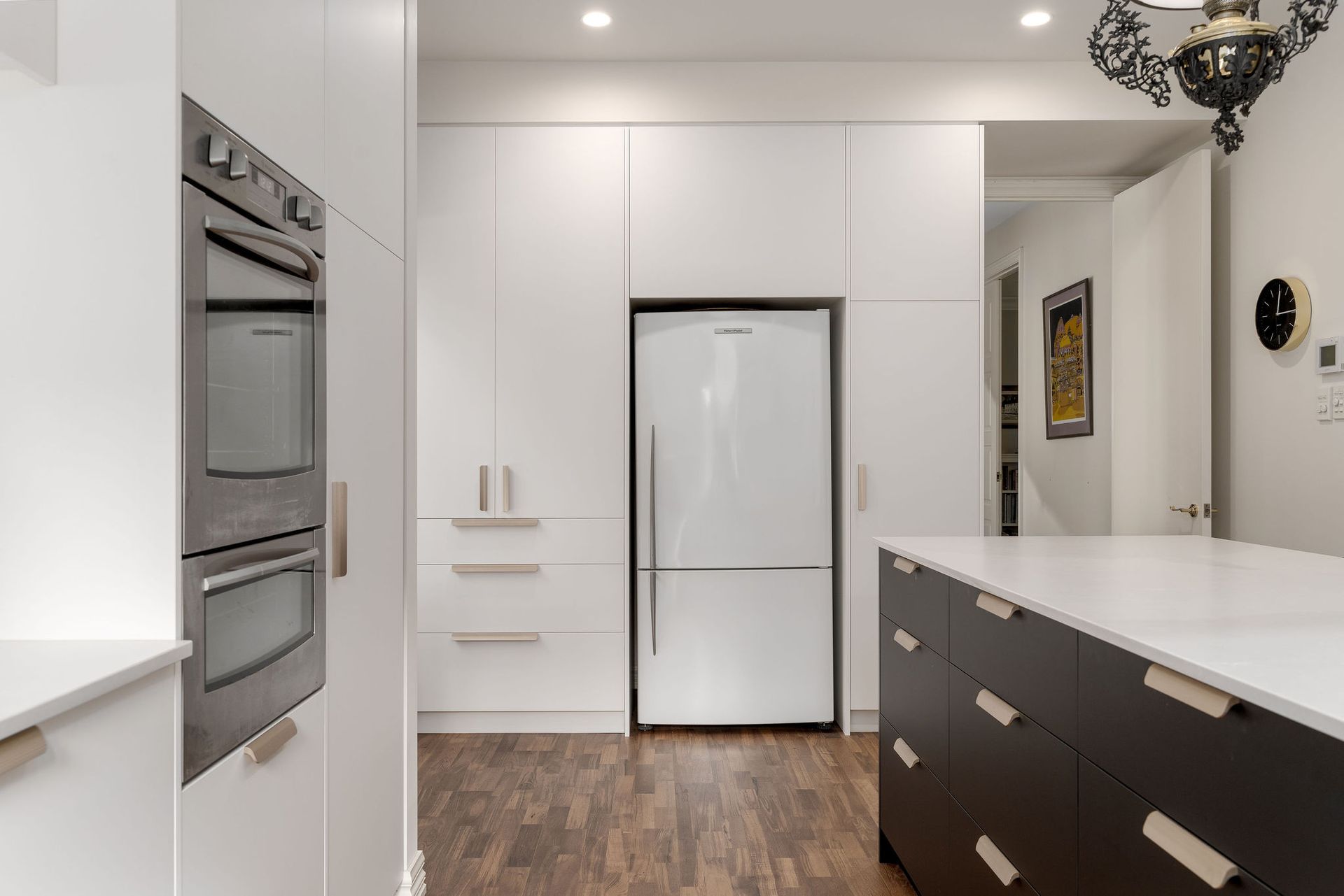 A kitchen with white cabinets , black cabinets and a white refrigerator.