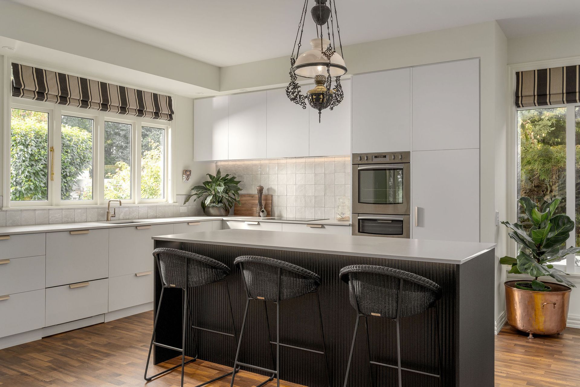 A kitchen with white cabinets , a large island , stools and a chandelier.