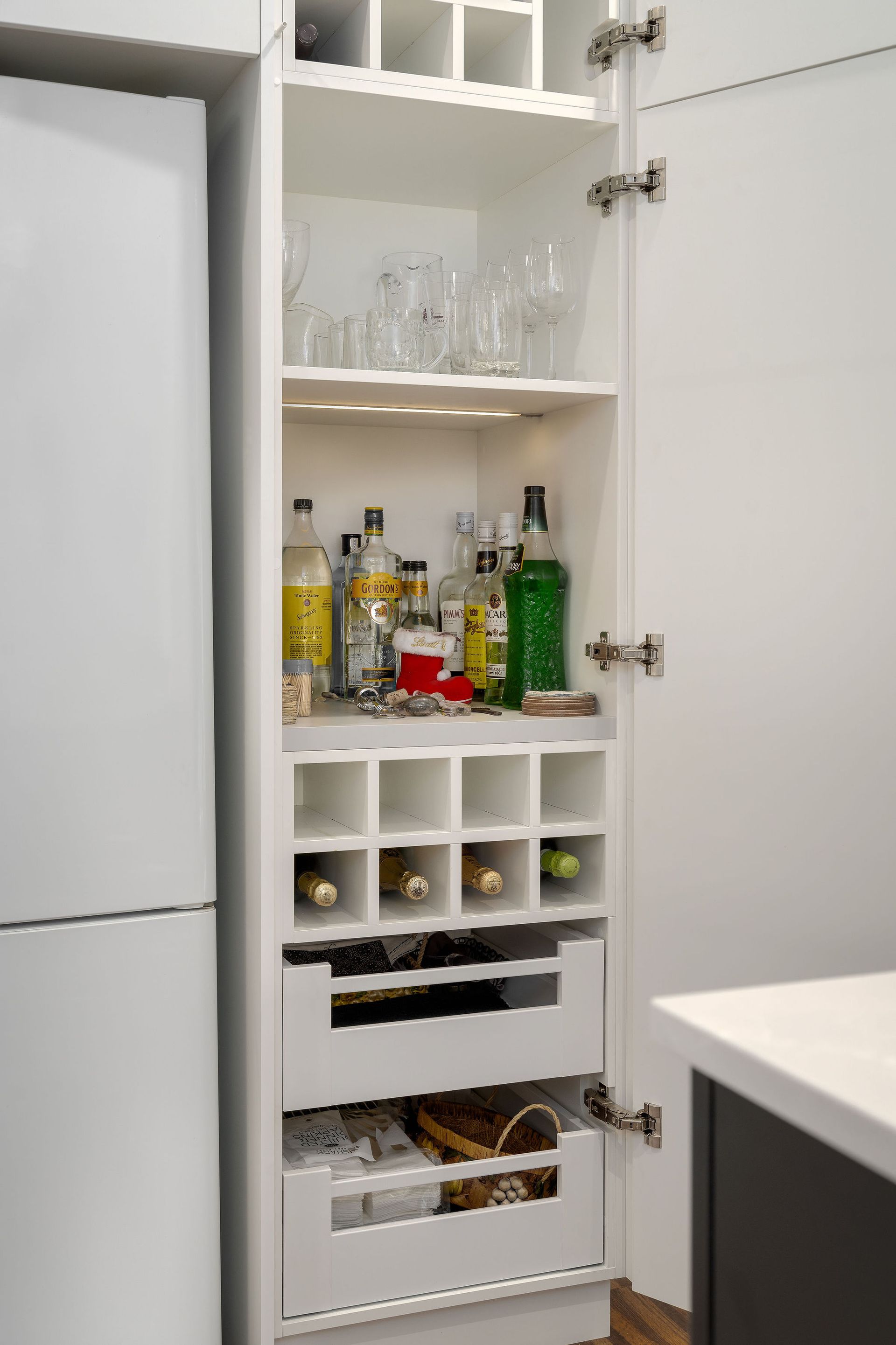 A kitchen cabinet filled with bottles and glasses and a wine rack.