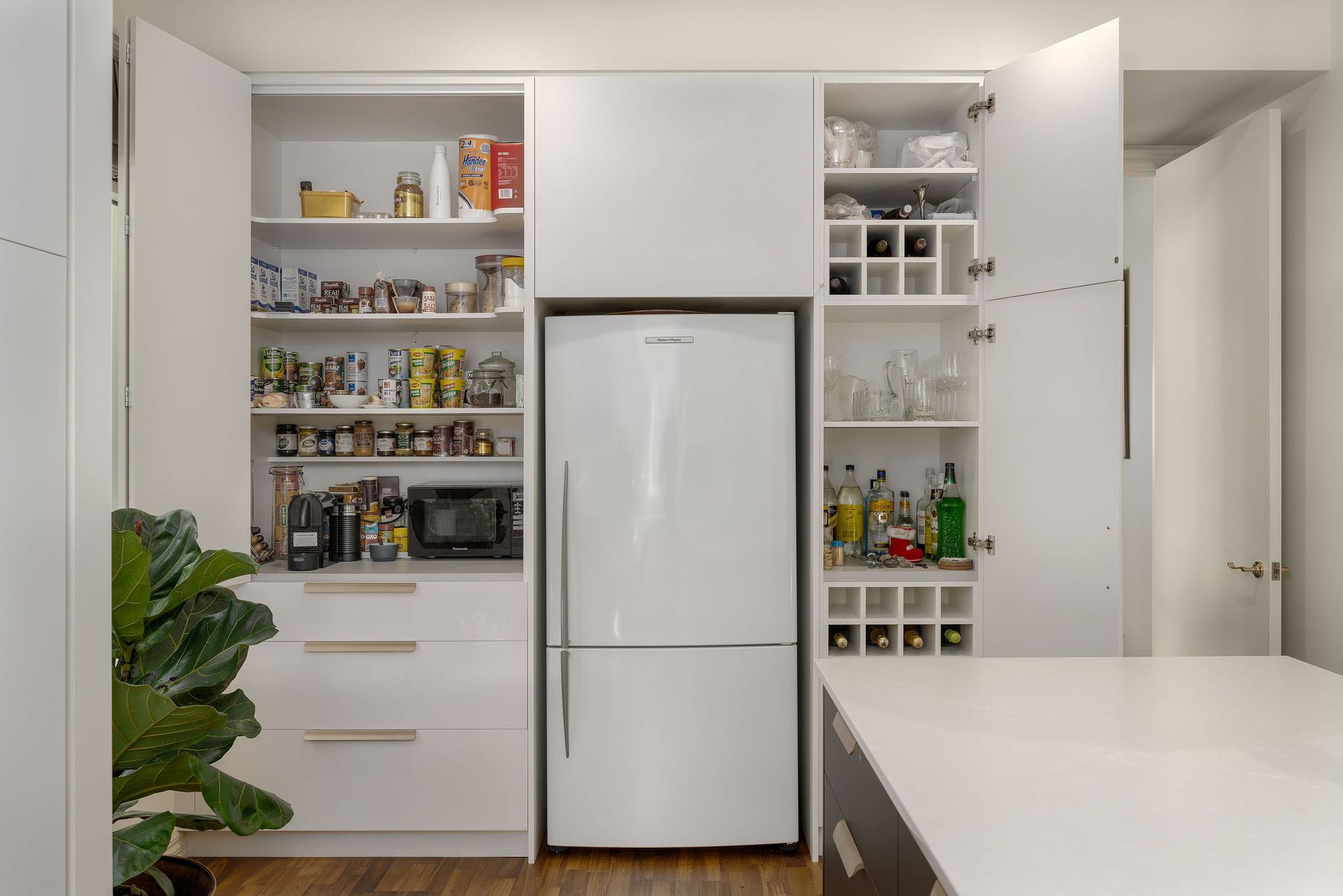 A kitchen with white cabinets , a refrigerator , a wine rack and a pantry.