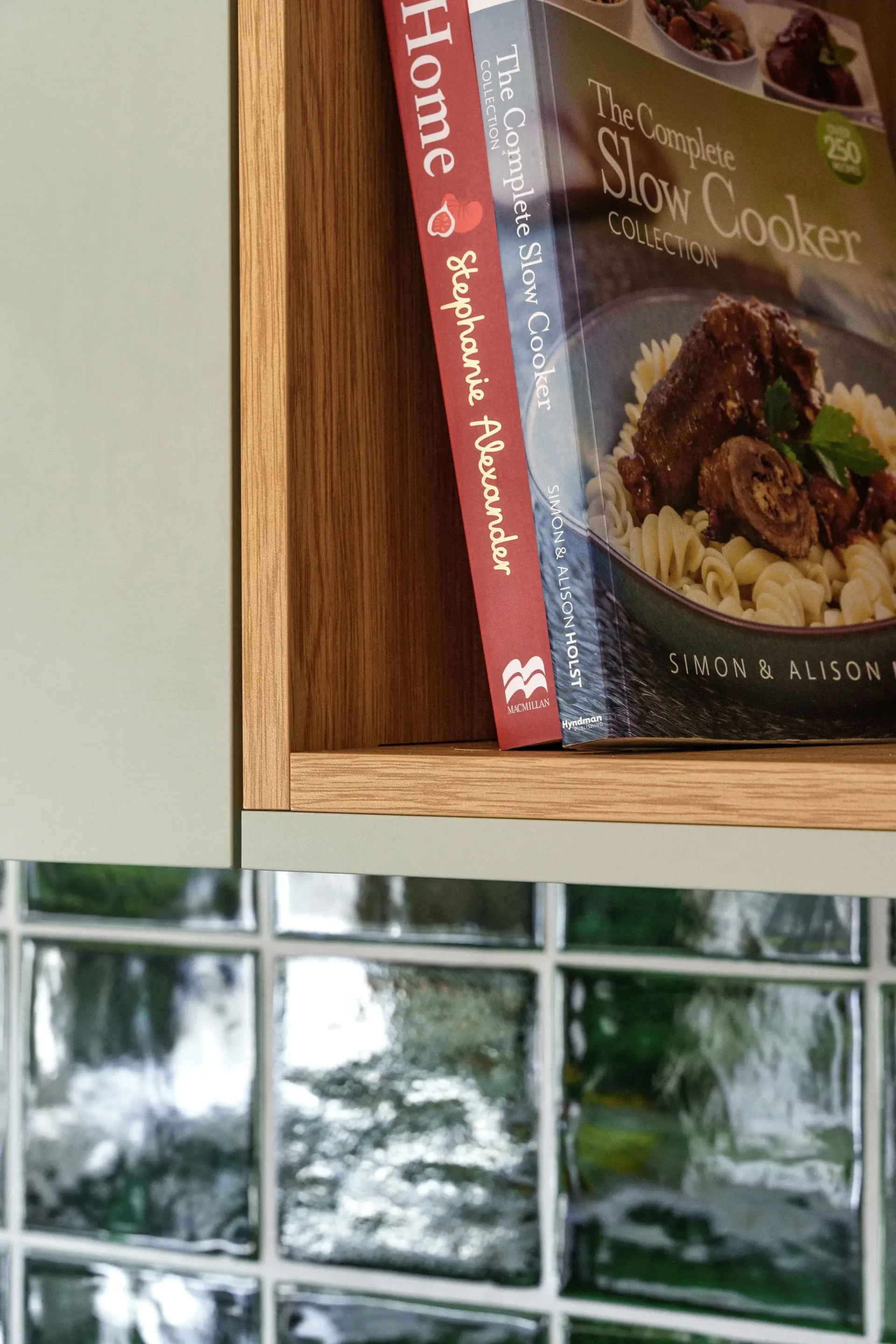 Three cookbooks are sitting on a wooden shelf.