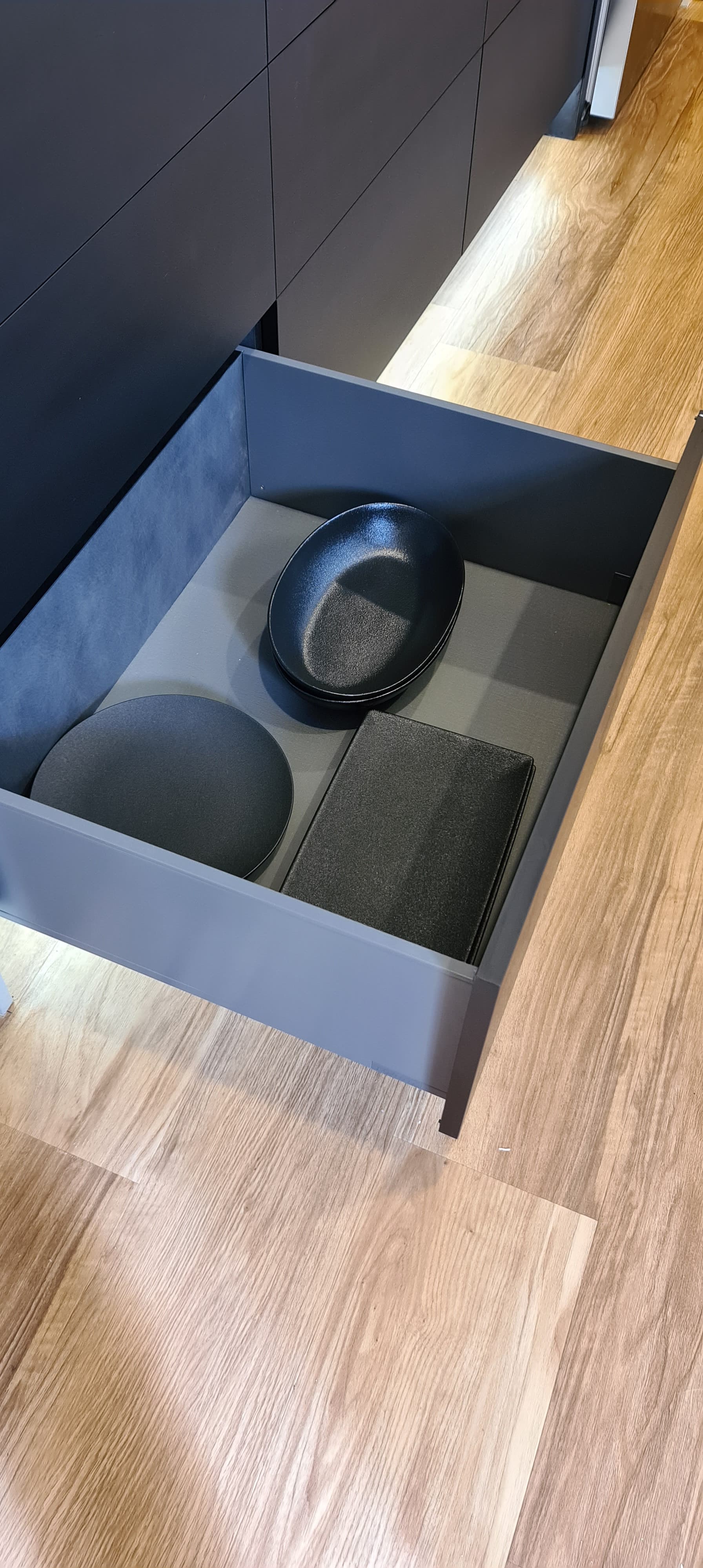 A drawer filled with plates and a bowl on a wooden floor.
