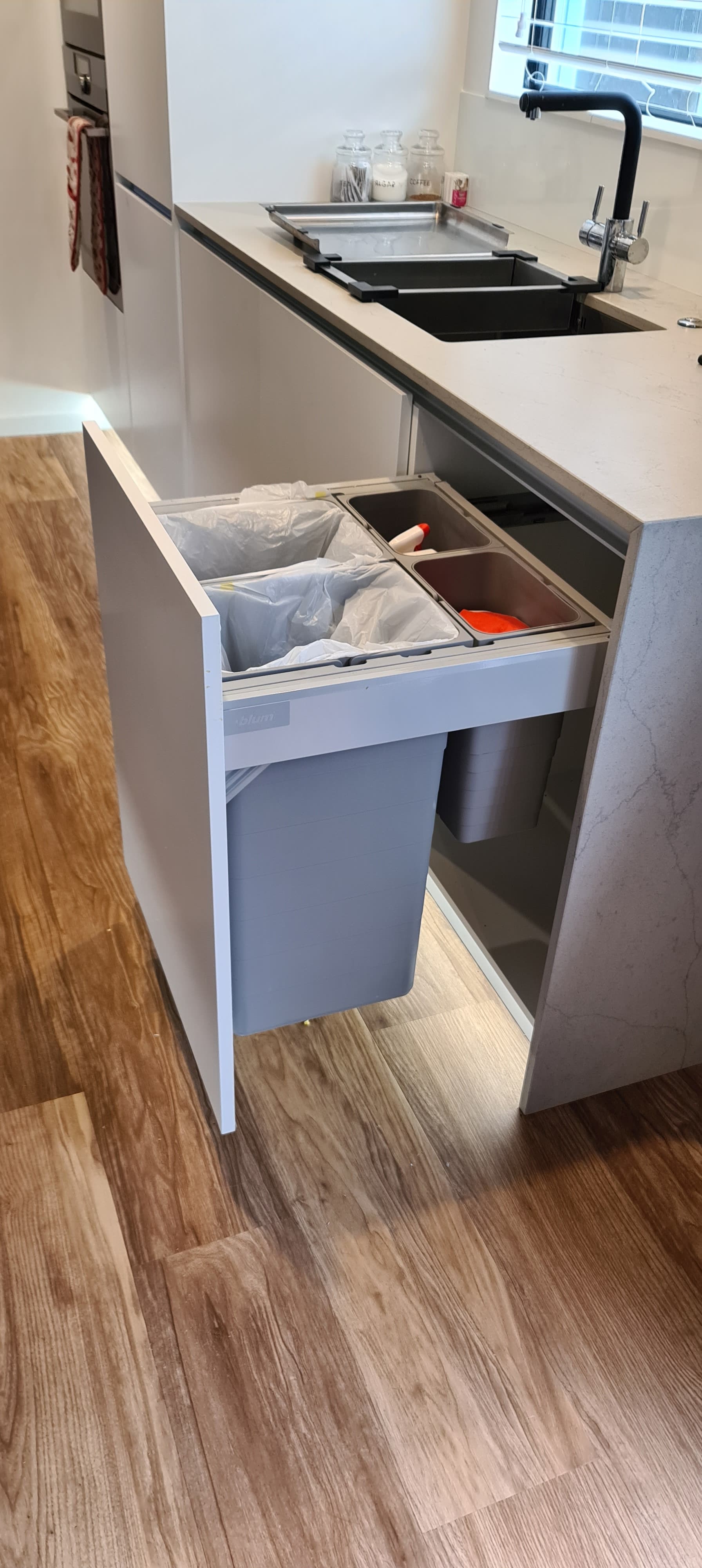 A kitchen with a sink and a trash can in a drawer.