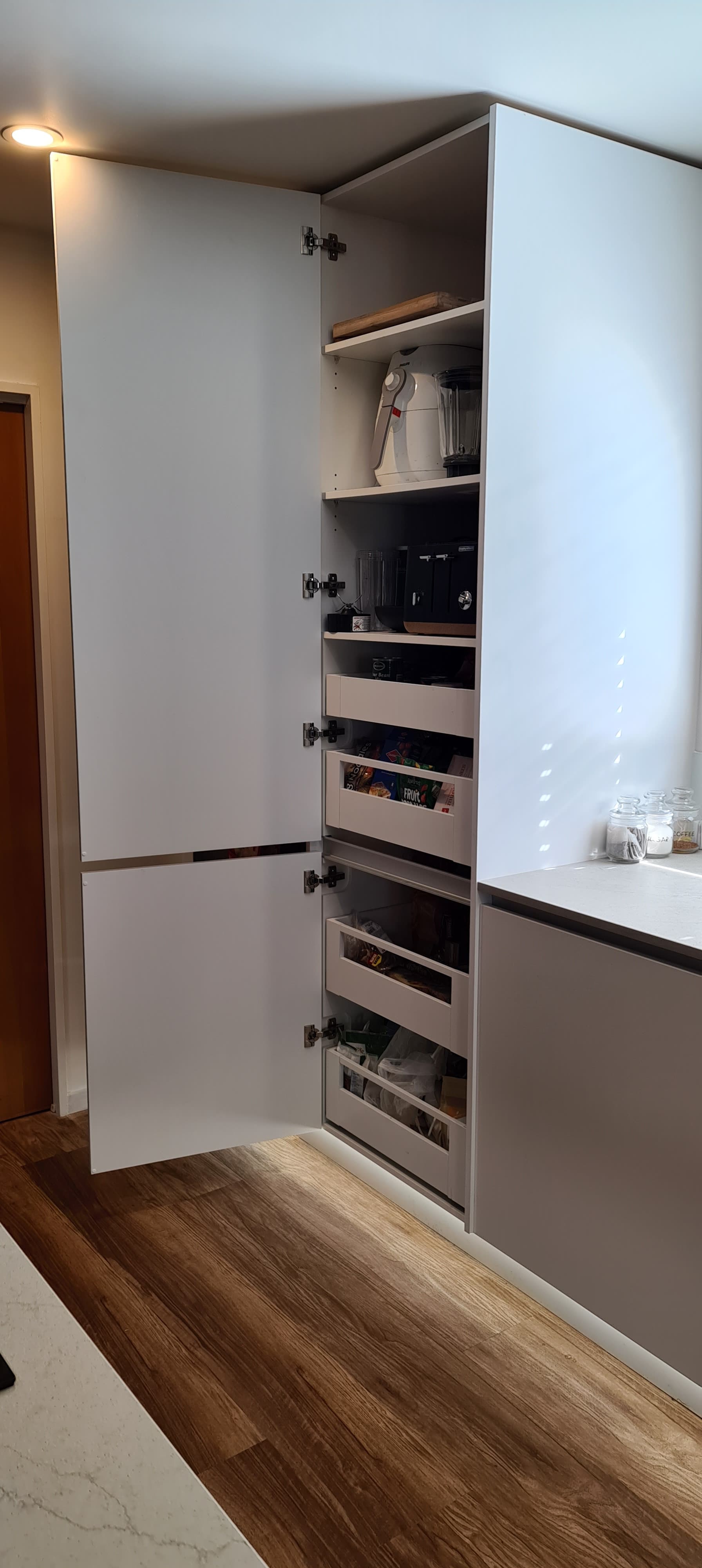 A kitchen with white cabinets and wooden floors and a refrigerator.