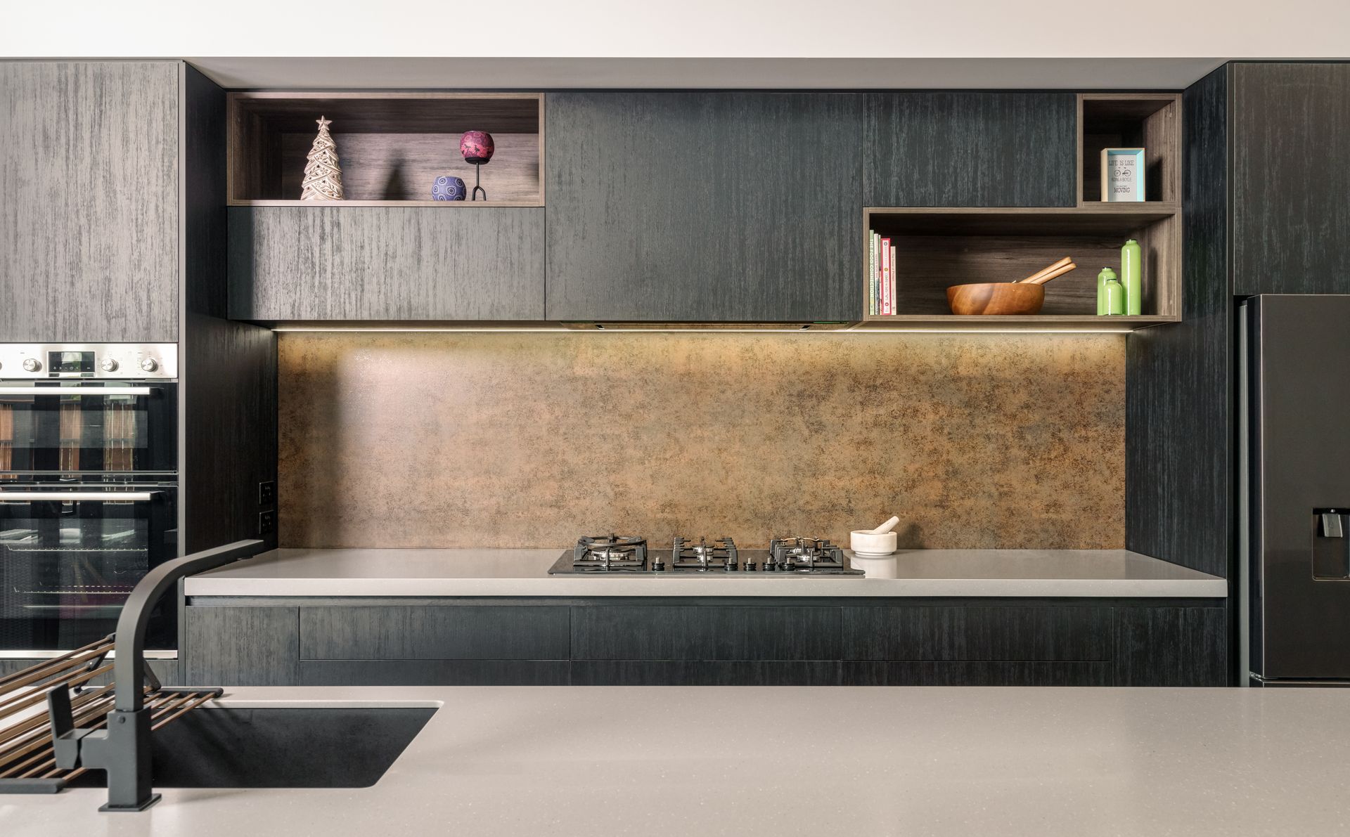 A kitchen with black cabinets , a sink , a refrigerator , and a stove top oven.