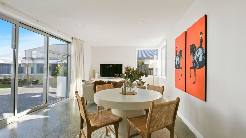 A dining room with a round table and chairs and a painting on the wall.