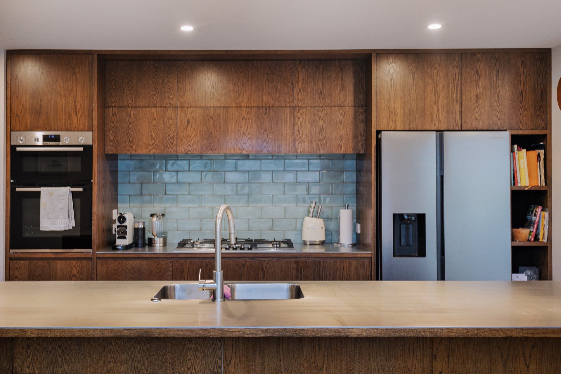 A kitchen with wooden cabinets , a stainless steel refrigerator , a sink , and a stove.