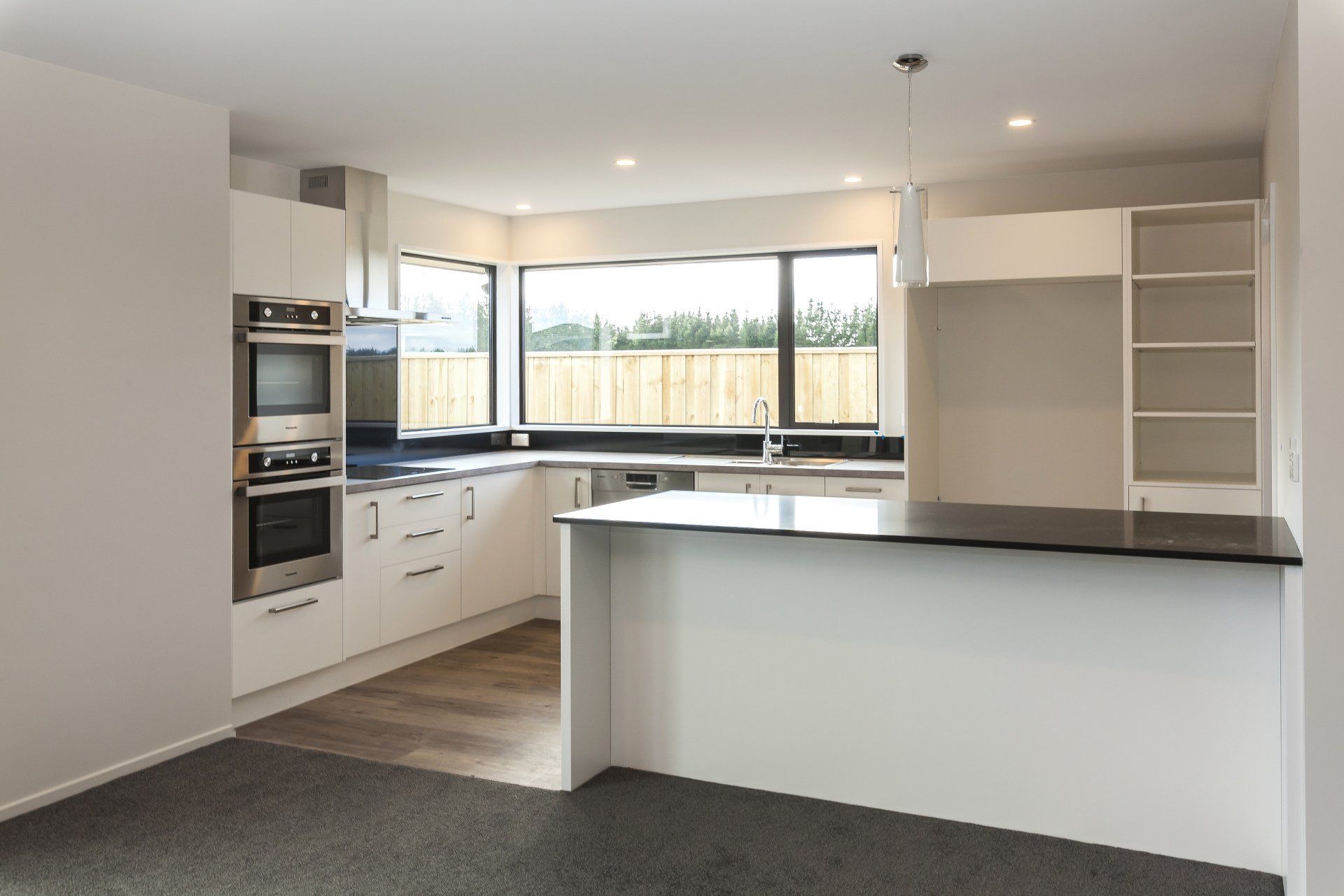 An empty kitchen with white cabinets and stainless steel appliances.