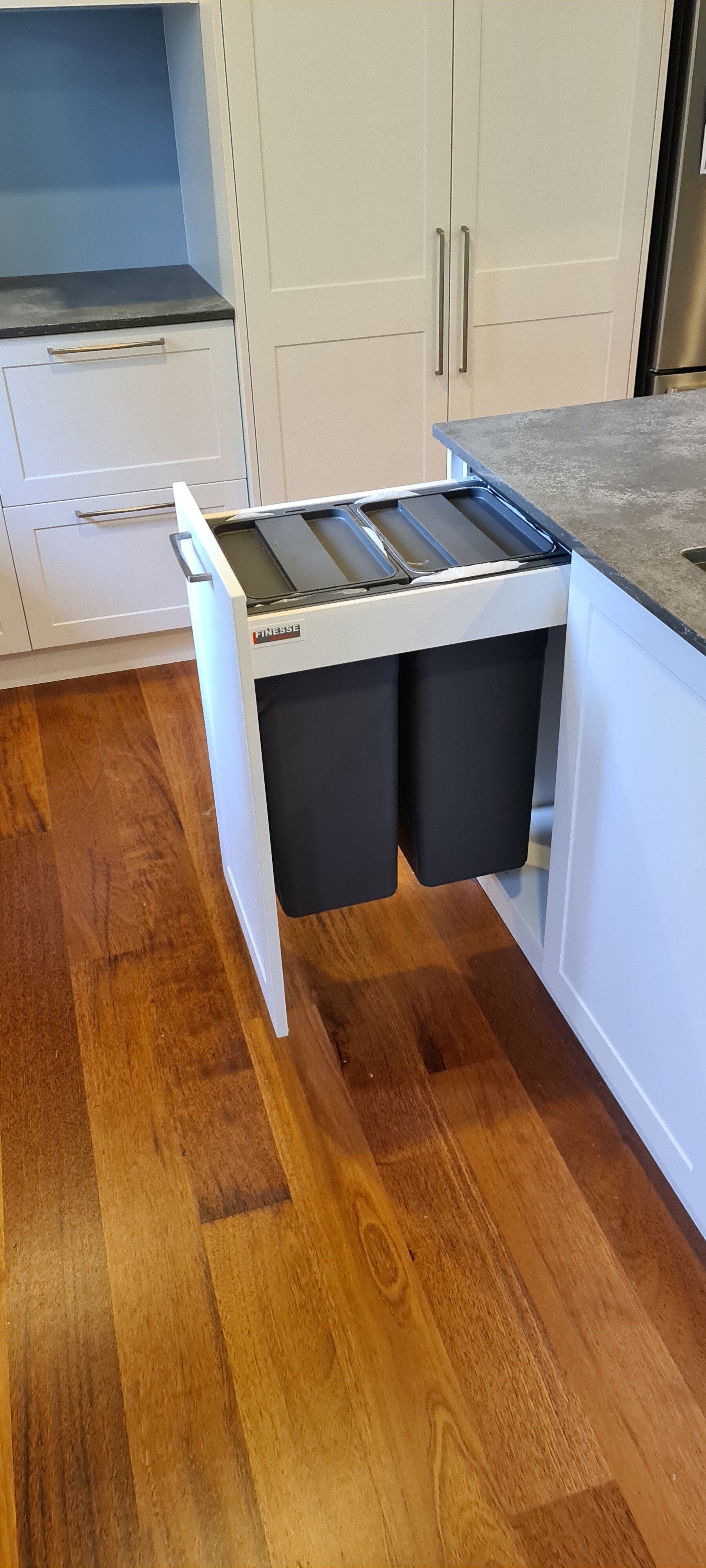 A kitchen with hardwood floors and a pull out trash can.