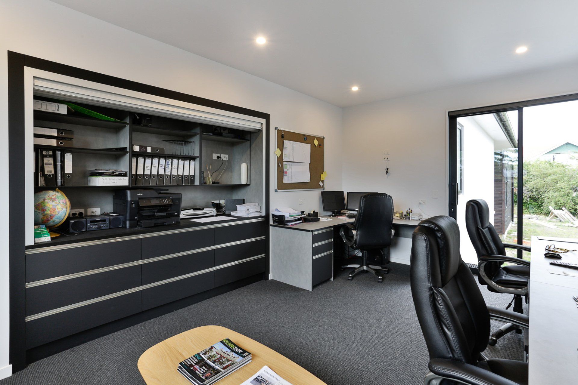 A home office with a desk , chairs , shelves and a coffee table.
