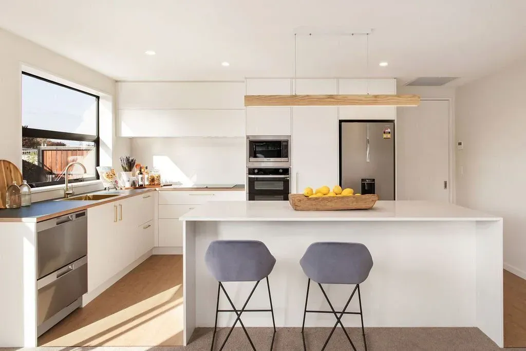 A kitchen with white cabinets , stainless steel appliances , a large island and two stools.
