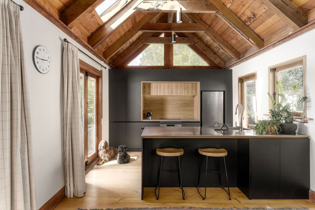A kitchen with a clock on the wall and a wooden ceiling.