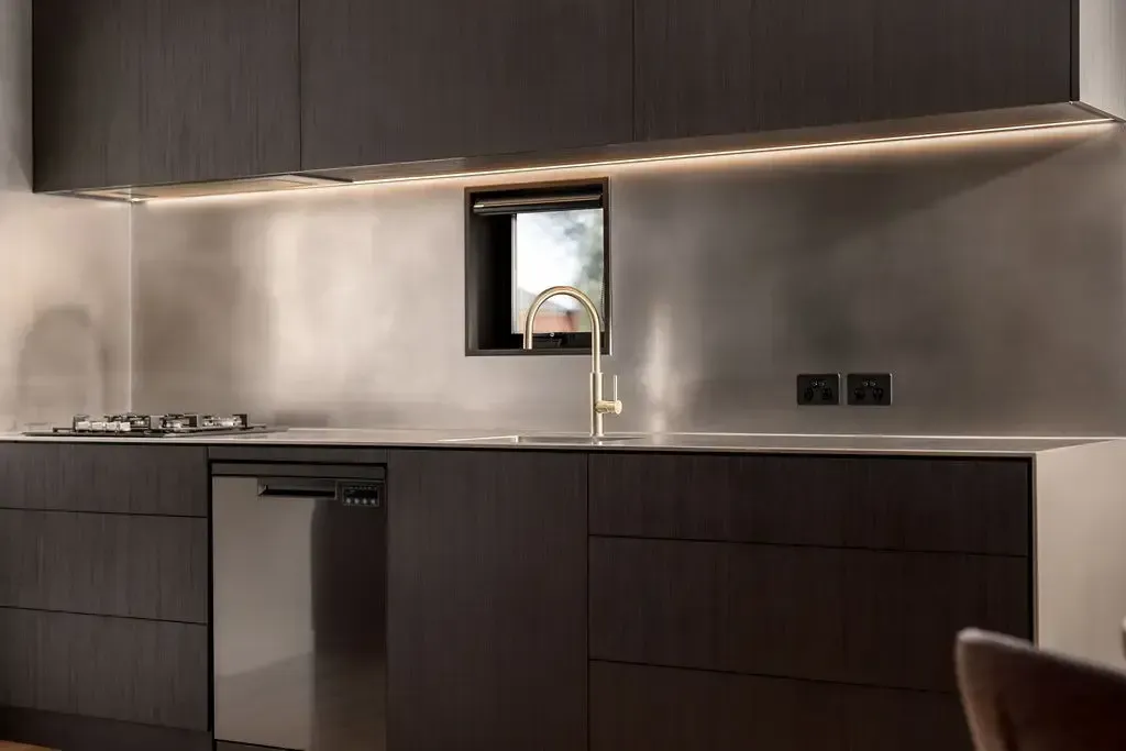 Modern kitchen with dark brown cabinets, stainless steel backsplash, and under-cabinet lighting.