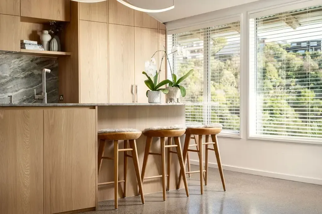 Kitchen with wood cabinets, bar stools, and a view of trees.