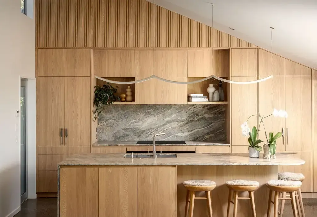 Wooden kitchen with island, cabinets, marble backsplash, and stools.