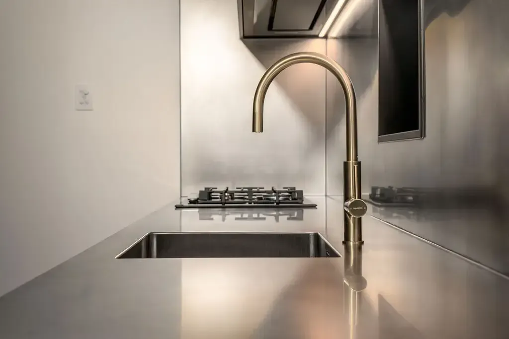 Stainless steel kitchen with gold faucet, stove, and sink; minimalist design.