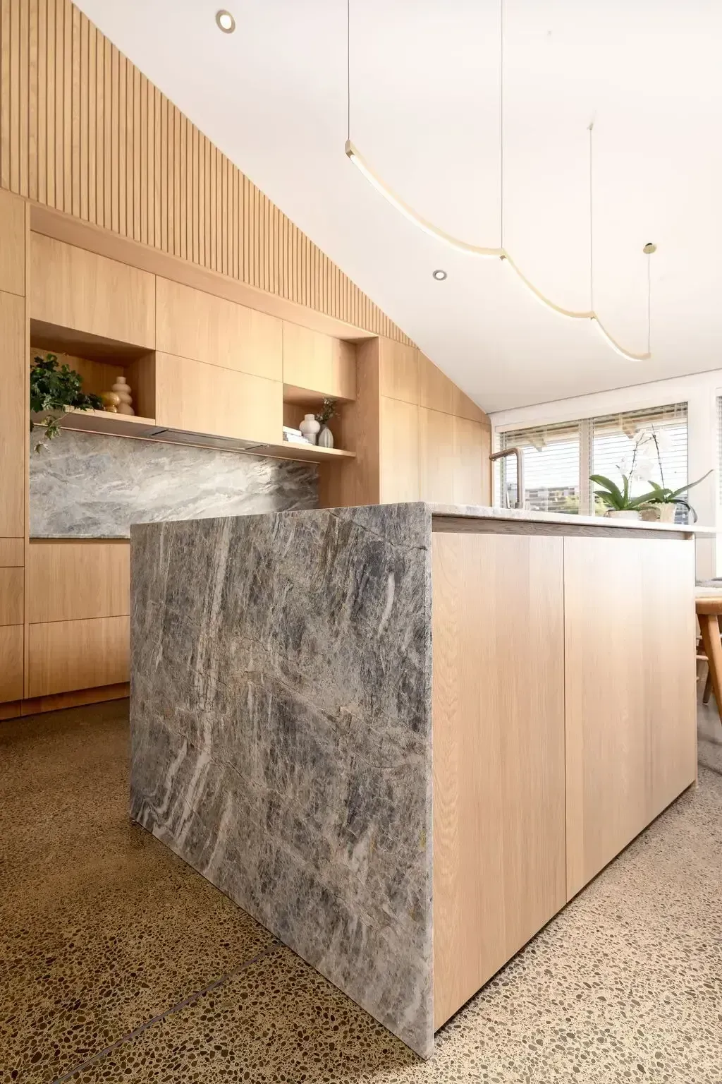 Modern kitchen with a gray marble island, light wood cabinetry, and a textured floor.