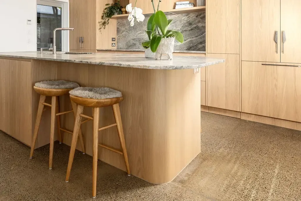Kitchen island with two stools, light wood cabinets, stone countertop, orchid, and concrete floor.