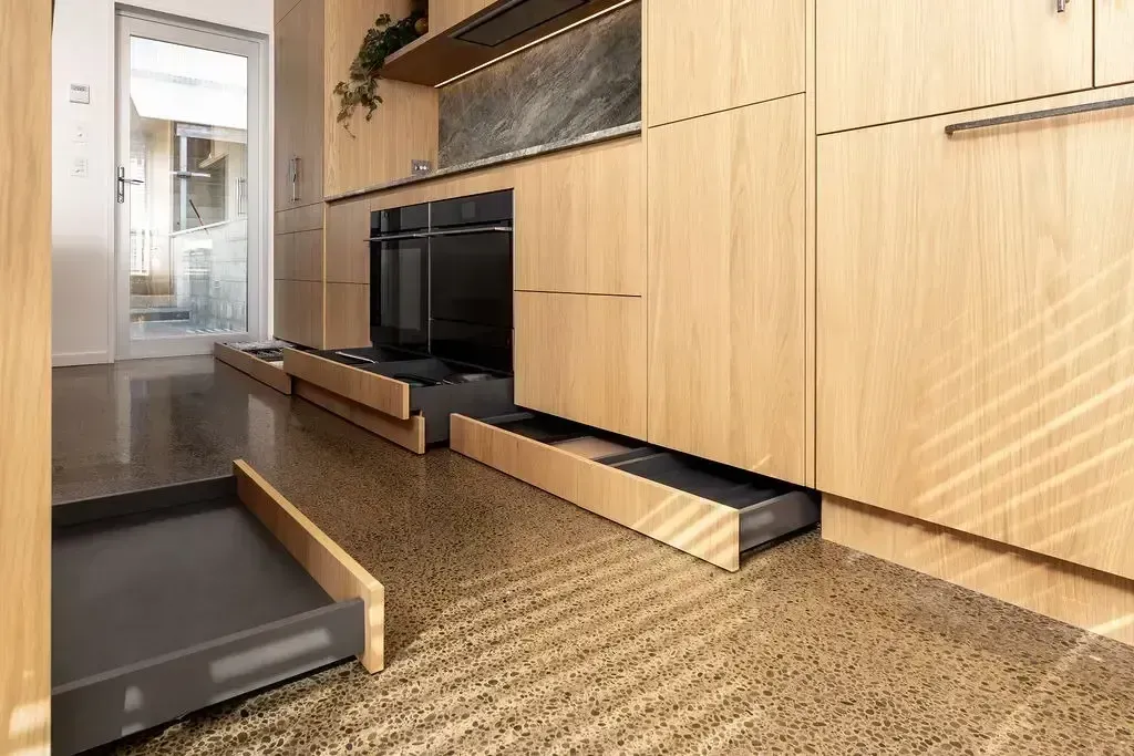 Wooden kitchen cabinets with open drawers, dark oven, and concrete flooring.
