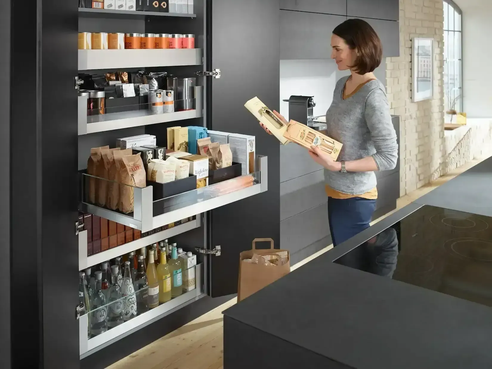 Woman reaching into a pull-out pantry, holding a box; kitchen with dark cabinets, stainless shelving.